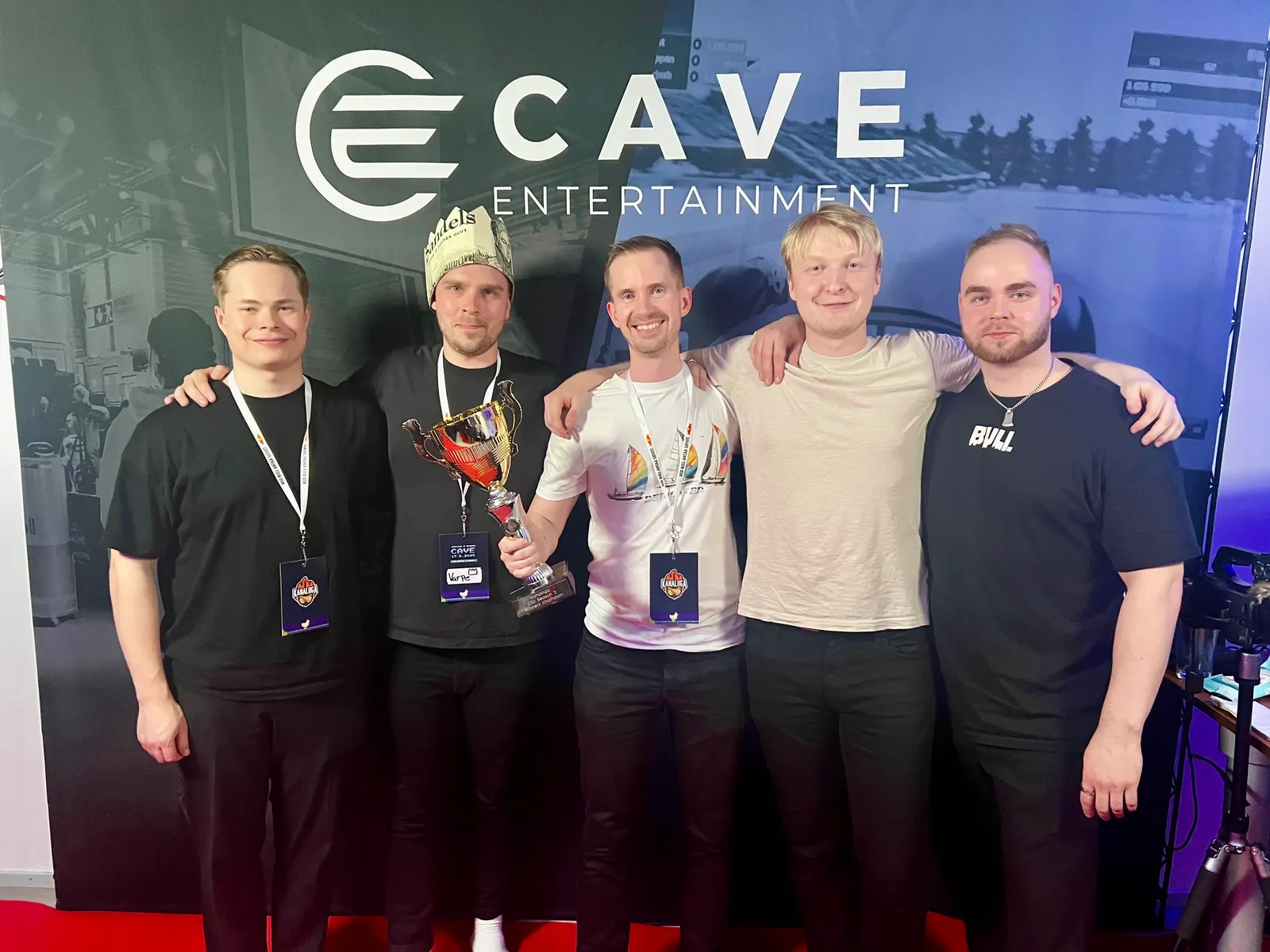 ALM Partnersin viisi pelaajaa Cave Entertainmentin taustaseinän edessä, yksi pitelee pokaalia.