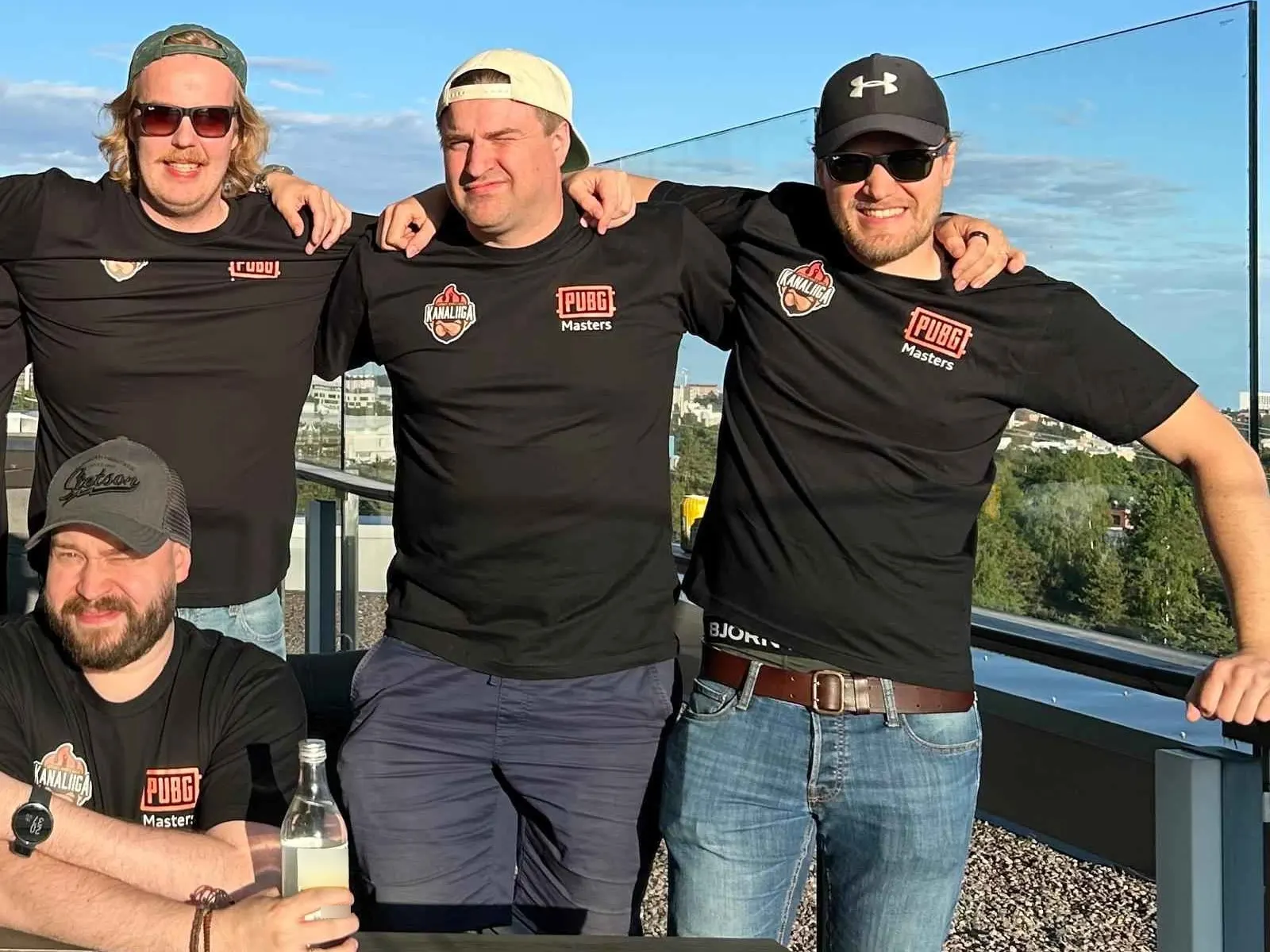 Neljä CGI Fyysinen Preesensin pelaajaa PUBG Masters -paidoissa kattoterassilla.