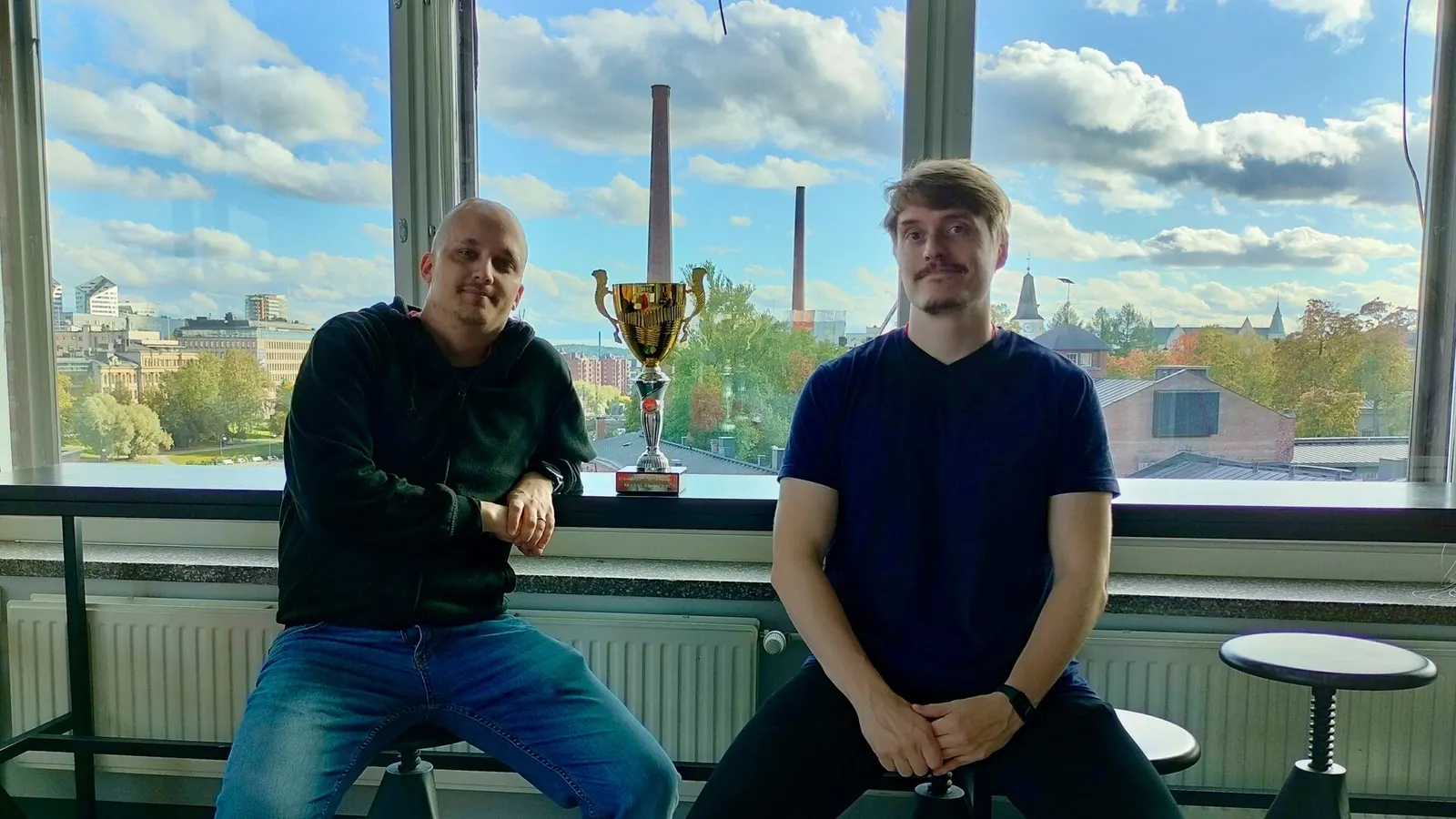 Digia Vengers' captain and vice-captain sitting by a window with the championship trophy between them.