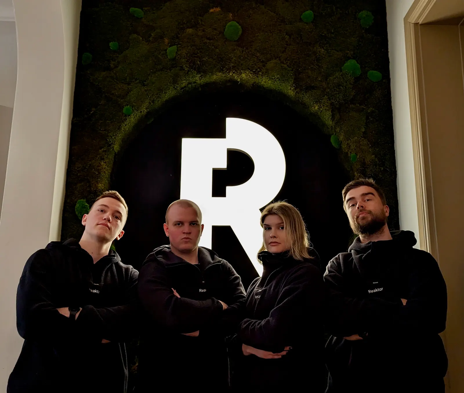 Reaktor Out of Åboostin neljä pelaajaa kädet ristissä Reaktorin logon edessä.